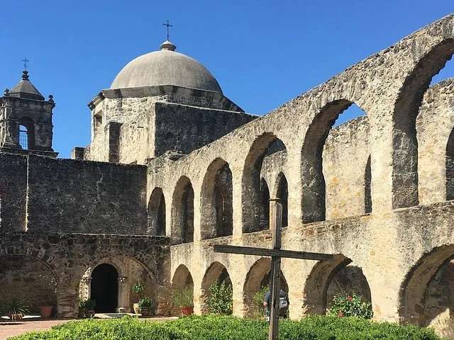 Mission San Jose courtyard with stone arches, dome, and a wooden cross