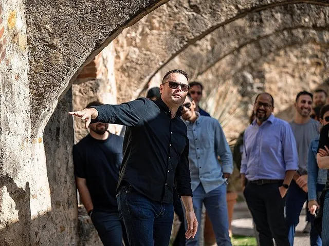 Tour guide pointing and talking to a group near stone arches