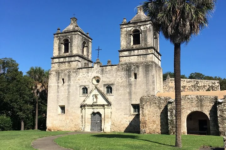 Mission Concepcion stone church with twin bell towers and a palm tree