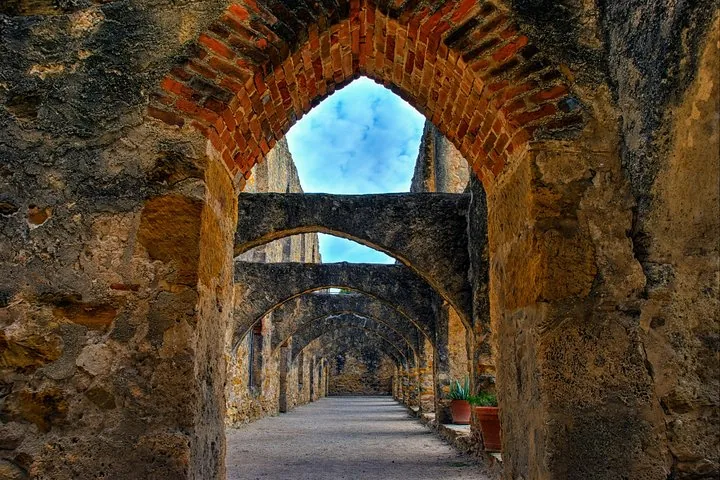 A series of stone arches forming a walkway in a mission ruin