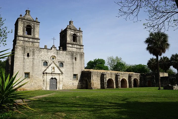 Mission Concepcion with its twin bell towers, arches, and a palm tree